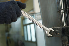 Silver combination wrench held in glove, open end gripping a metal fastener