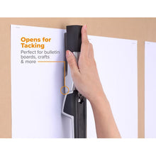 Hand using a handheld stapler to tack paper to a board