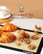 Black silicone baking mat with croissants, cookies, and utensils on top.