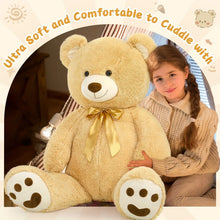 Large tan teddy bear plush with bow, stitched face, and rounded paws