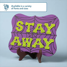 Wooden letter sign reading “STAY AWAY”, green letters with spiderweb design