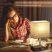Lit fabric-shade bedside lamp with black charging dock and phone charging cables