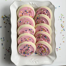 Pink frosted sugar cookies with multicolor sprinkles, stacked in a white tray