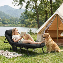 Black folding camping cot with cushioned seat and rounded headrest beside tent
