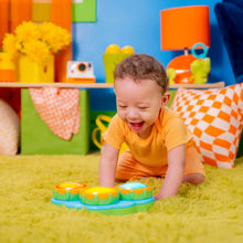 Child reaching toward a green musical drum toy with three colorful drum pads