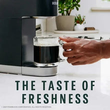 Keurig mug filled with dark coffee and foam, held under a pour; freshness text visible