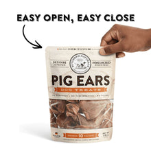 Pig ears dog treats pouch held by a hand, smoked chews visible through window