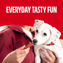 Soft dog treat held near a white spotted dog’s mouth with a red collar