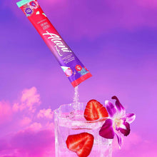 Energy drink powder stick pouring into a glass beverage with strawberry pieces