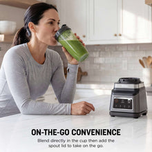 Blender on countertop with green smoothie in a grab-and-go cup and pitcher