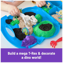 Blue sand tray with white dinosaur fossil pieces, green and black sand, red tool