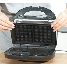 Open black waffle and sandwich maker with two textured plates held by hands