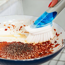 Dishwashing brush with blue handle scrubbing brown grit off a pan surface