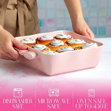 Pink square ceramic baking dish with bow handles holding frosted cinnamon rolls