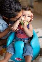 Infant chewing a green textured teether while seated in a seat
