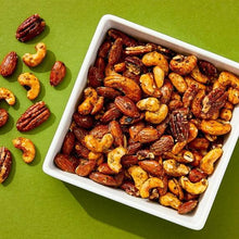 Seasoned mixed nuts in a white serving dish with scattered nuts around