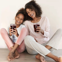 Two people holding dark grape juice bottles, smiling on a living-room couch