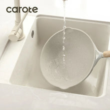 Nonstick frying pan with light wood handle, rinsed with a water stream.