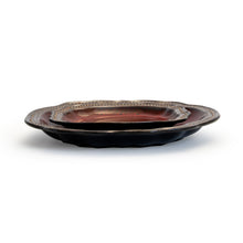 Shallow red stoneware bowl set with scalloped edges and dark underside