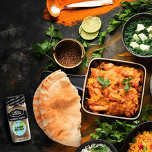 Garam masala seasoning blend jar with curry dish, naan, and chopped herbs on table