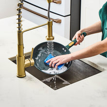 Nonstick skillet rinsed under sink faucet, dark green handle visible