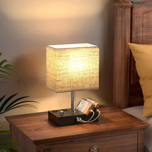 Fabric-shade bedside lamp with lit shade and black charging base on a wooden table