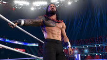 Wrestler standing in ring wearing black pants with long arm tattoos