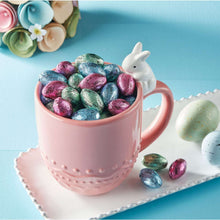 Pink mug filled with wrapped milk chocolate Easter candy eggs and a white bunny