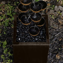 Square reservoir of black water with bronze-rim cups and falling streams