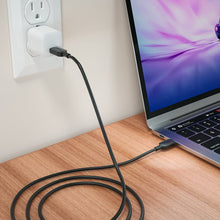 USB-C charging cable plugged into wall outlet and laptop, black cable