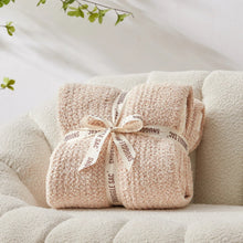 Beige throw blanket tied with a fabric ribbon, showing knitted texture and cream border.