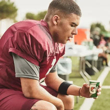 Athlete holding a sports drink bottle while sitting on the field