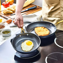 Black speckled non-stick fry pan with gold handle, cooking a fried egg and pancake.