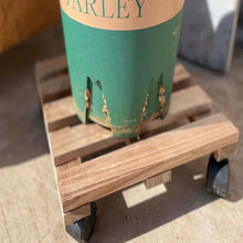 Wooden plant caddy holding a teal pot, with caster wheels underneath.
