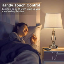 Bedside table lamp with white linen shade and brushed metal base, lit with touch control