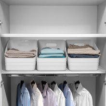 White plastic slanted storage bin on closet shelf holding folded clothes