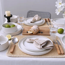 White stoneware dinnerware set with stacked plates and bowls on woven placemat