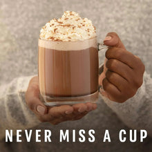 Glass mug of hot cocoa with whipped cream topping held in a cupped hand