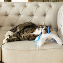 Electronic cat toy with blue wand and fluffy feather swatter attached to a white curved base