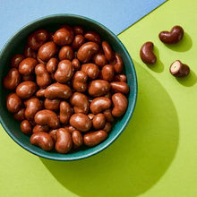Chocolate-coated cashews in a bowl with scattered pieces
