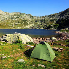 Green camping tent pitched outdoors near a rocky lake shore