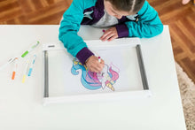 Child drawing on a white LED light board with colored crayons