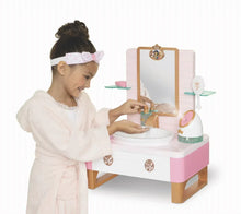 Child in white robe using a pink play vanity sink with mirror and bottles