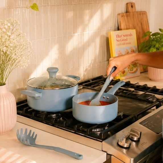 Blue ceramic non-stick sauce pan on stovetop with lid and spatula