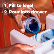 Detergent poured into a washing machine drawer from a blue-capped bottle.