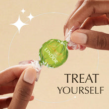 Hands unwrapping a green Lindor pistachio chocolate truffle candy