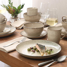 Cream stoneware dinnerware set on table, bowls, plates and mugs with glassware