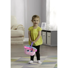 Toddler holding pink toy picnic basket with purple handle and face design