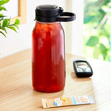 Iced tea drink mix packets beside a red bottle with black lid on a table