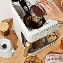 Electric blade coffee grinder with its lid removed beside a coffee maker